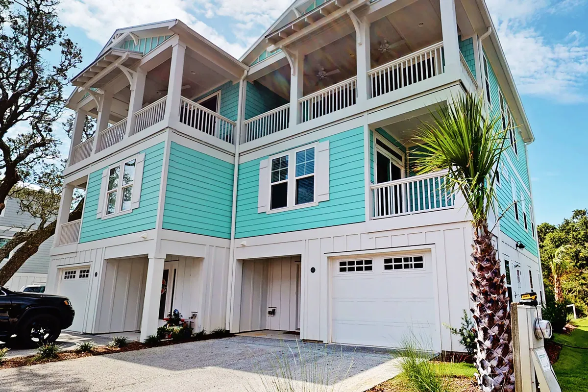 The exterior of a contemporary, turquoise home with spacious balconies, palm trees, and a sunny driveway. The scene hints at cheerful family gatherings, outdoor dining, and relaxation on the balconies, reinforcing the modern and vibrant community atmosphere.