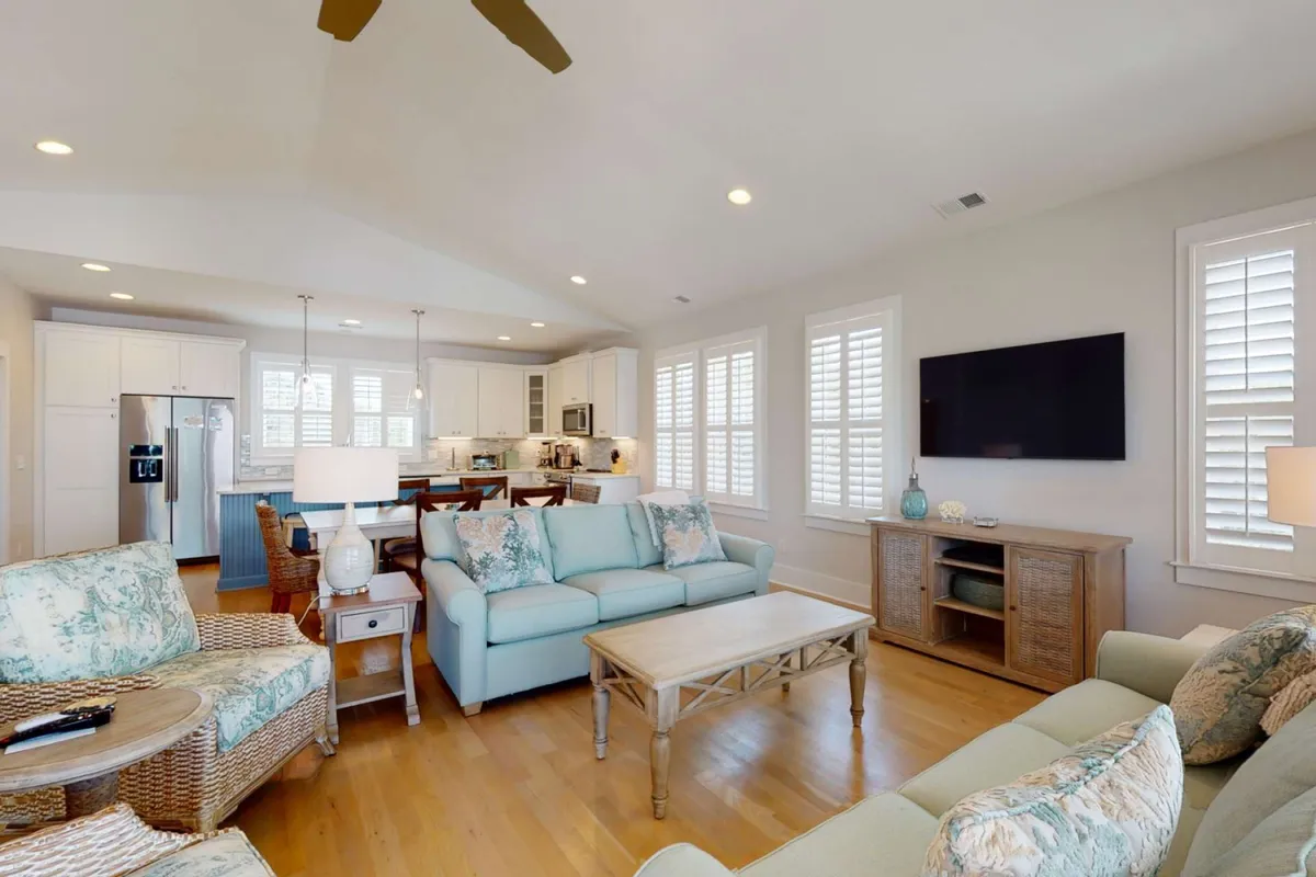 A cozy view of the living area with a light blue sofa and recliner centered around a wooden coffee table, with the kitchen area visible in the background. This angle conveys comfort and togetherness, suggesting a perfect spot for relaxing, movie nights, and informal conversations.