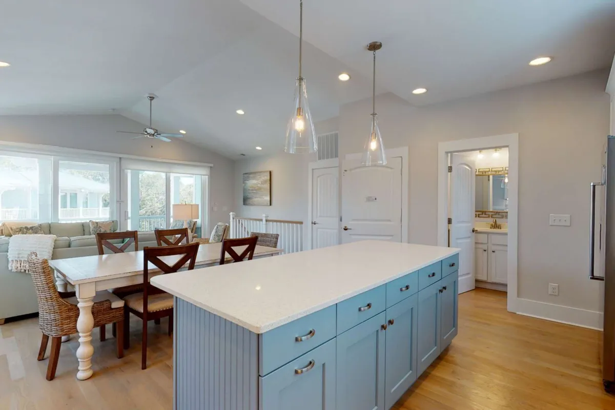 This interior shot focuses on the kitchen island, dining table, and the bright, airy quality of the space thanks to large windows and stylish lighting. The setup invites gatherings for meals or conversation in a relaxed, elegant setting.