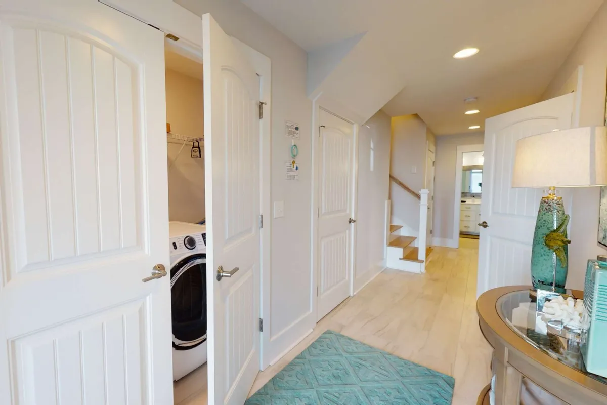 A welcoming interior scene featuring the entryway, decorative lamp, entryway table, and a glimpse of the laundry area and staircase. The setting feels inviting and signals a thoughtfully designed, easy-to-navigate environment from the moment you step inside.