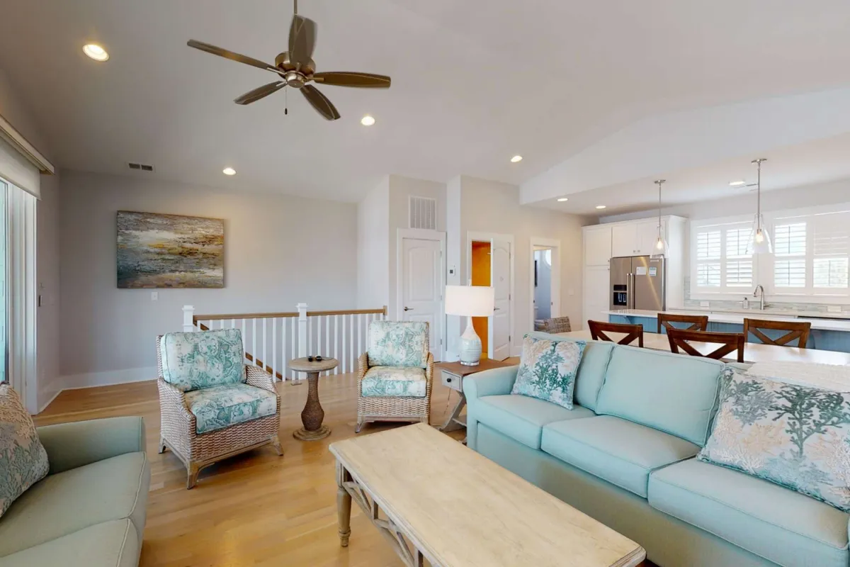 A welcoming interior living area that includes a sofa, armchairs, coffee table, and an open kitchen in the background. The space is arranged for socializing and entertaining, bathed in natural light for an inviting atmosphere.