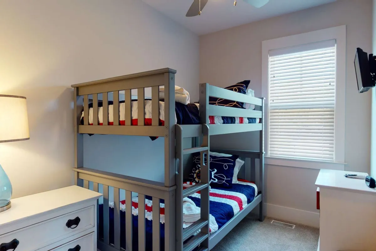 A cheerful bunk room is depicted with two twin bunk beds, a nightstand with a lamp, and playful decorative pillows. The atmosphere is both playful and cozy, designed to delight younger guests and provide a fun sleeping arrangement.